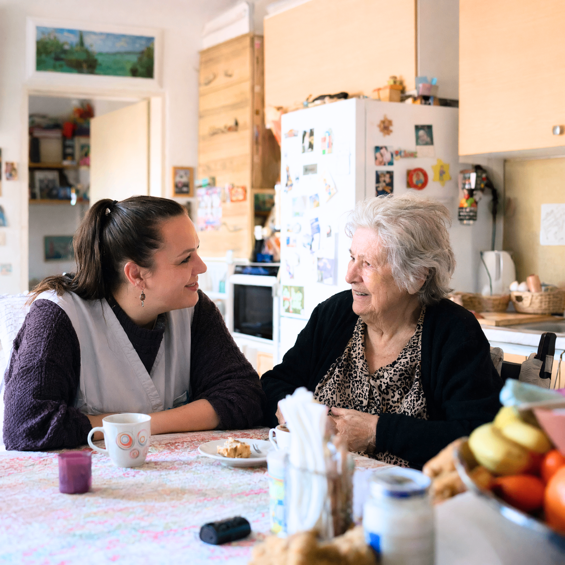Betreuungskraft im Gespräch mit einer Seniorin am Küchentisch